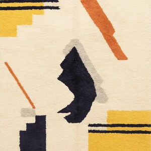 Puede incluir: Alfombra color crema con un dise&ntilde;o abstracto. La alfombra presenta formas geom&eacute;tricas en azul marino, amarillo, naranja y gris. El dise&ntilde;o incluye rect&aacute;ngulos, l&iacute;neas y formas angulares, creando una est&eacute;tica moderna. La alfombra tiene una superficie texturizada.