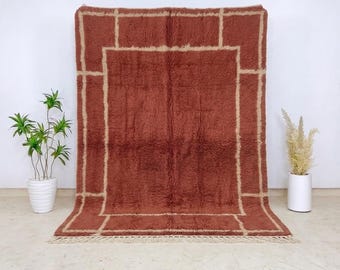 May include: A rectangular area rug featuring a deep terracotta red base color with a contrasting cream-colored geometric grid pattern. The rug has a thick, shaggy pile texture and includes short, cream-colored fringe along the bottom edge.