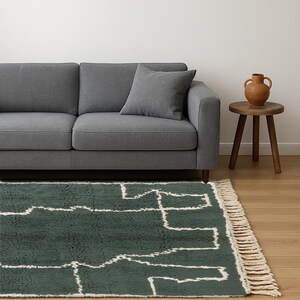 May include: A dark green rug with a white geometric pattern and fringe detail. A gray sofa with a matching pillow is in the background, along with a small wooden side table and a terracotta vase.