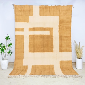 Plush Moroccan wool rug with a minimalist camel and cream grid pattern, hand-knotted by Berber artisans using traditional techniques. This high-quality wool carpet offers a soft, dense texture underfoot and a modern, structured design perfect for contemporary or Scandinavian interiors. The clean geometric lines and neutral palette make it a versatile floor covering for living rooms, dining areas, or elegant minimalist bedrooms seeking warmth and artisanal charm.