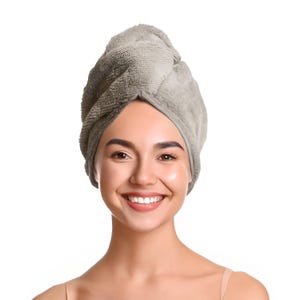 Pode incluir: Uma toalha de cabelo de microfibra cinza claro enrolada na cabeça de uma pessoa. A toalha foi projetada para absorver água e reduzir o tempo de secagem. A pessoa está sorrindo, com um fundo branco.