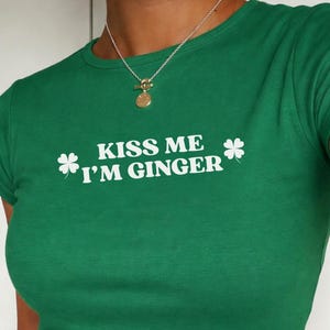 May include: A green crop top with the white text "KISS ME I'M GINGER" and shamrock graphics. The top is worn with dark grey denim jeans.