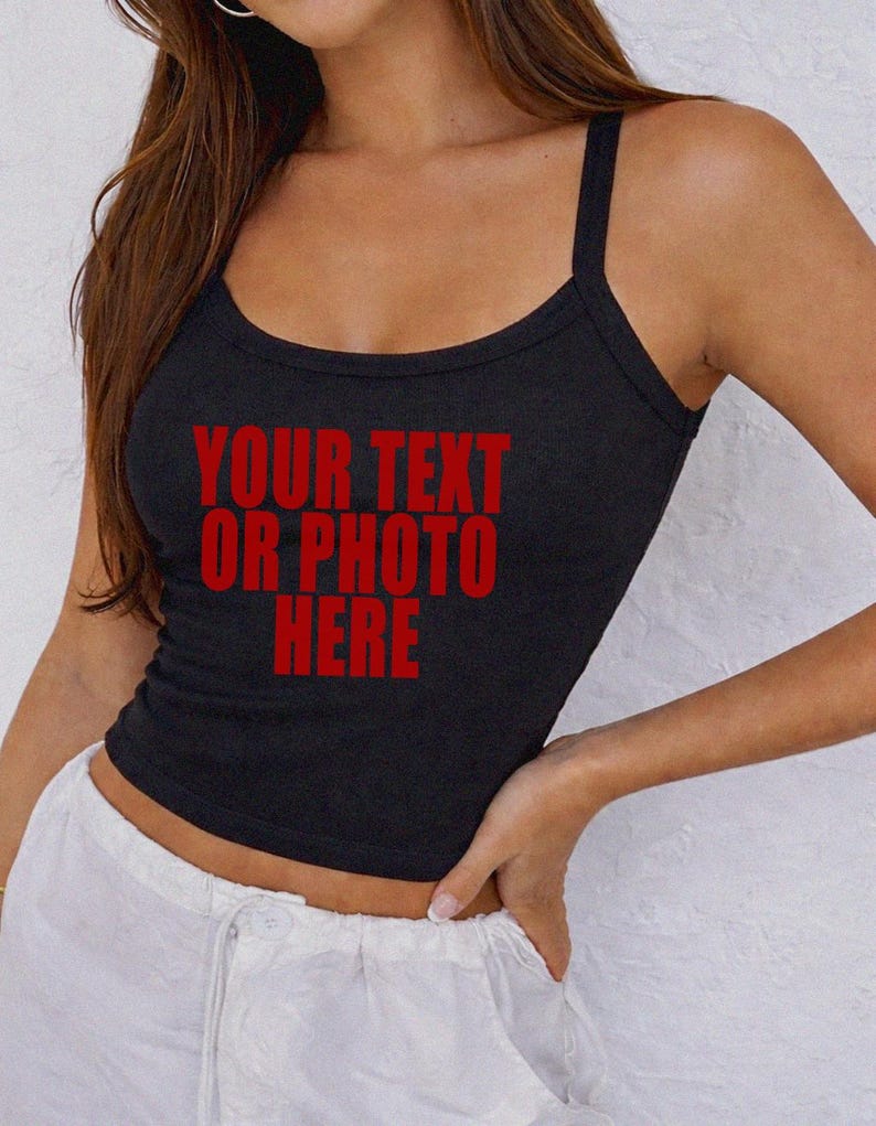 May include: A black ribbed tank top featuring a scoop neckline and thick shoulder straps. The center of the garment displays the red text "YOUR TEXT OR PHOTO HERE" in a bold, sans-serif font, indicating a customizable area for personal designs.
