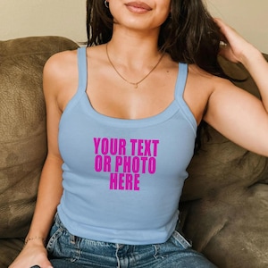 May include: A light blue tank top with a scoop neckline and thick shoulder straps. The center of the chest features the text "YOUR TEXT OR PHOTO HERE" printed in a bold, bright pink sans-serif font across three lines.