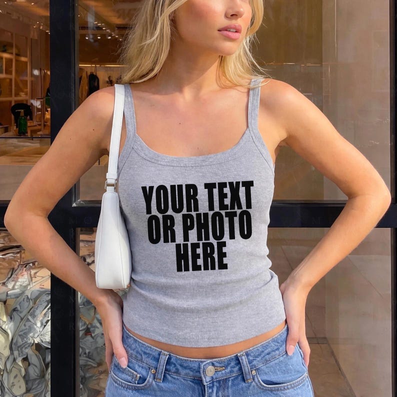 May include: A heather gray ribbed tank top with a scoop neckline and thick shoulder straps. The front of the garment features the black printed text "YOUR TEXT OR PHOTO HERE". A white shoulder bag with a thin strap is worn over one shoulder.