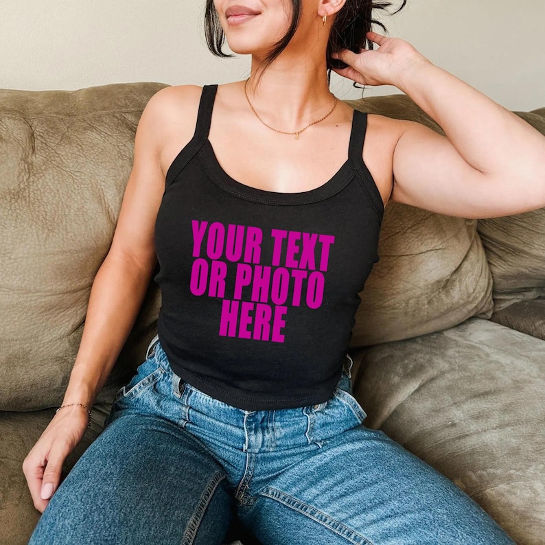 May include: A black sleeveless tank top with a scoop neckline and thick shoulder straps. The front of the garment features the text "YOUR TEXT OR PHOTO HERE" printed in a bold, bright magenta pink color across the center of the chest area.