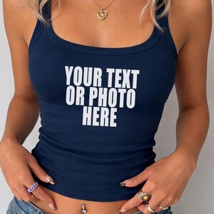 May include: A dark navy blue sleeveless tank top with a scoop neckline. The front of the garment features the white printed text "YOUR TEXT OR PHOTO HERE" centered on the chest. The top is paired with blue denim jeans.