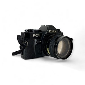 May include: A black Konica FC-1 35mm film camera with a silver lens. The lens says "Lens Made in Japan 50mm 1:1.8".