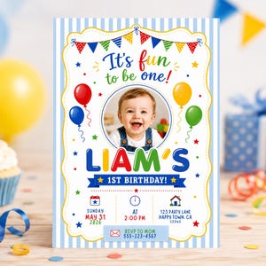 Puede incluir: Una invitación de cumpleaños a rayas azules y blancas con el texto "It's fun to be one!" y "Liam's 1st Birthday!". Una foto de un bebé sonriente está en el centro. La invitación incluye detalles de la fiesta e información RSVP.