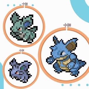 May include: Three cross-stitch embroidery hoops featuring pixelated images of a Pokemon character. The designs include a green and blue creature, a blue and brown creature, and a purple and blue creature, all set against a white background.