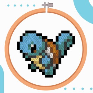 May include: A cross-stitch embroidery of a blue and brown pixelated turtle character, set within an orange embroidery hoop. The design is on a white background, with blue and orange geometric shapes in the corners.
