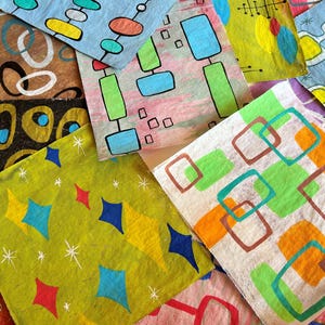 May include: A selection of patterned paper squares with mid-century modern designs. The squares display geometric shapes, including diamonds, rectangles, and circles, in various colours like blue, green, yellow, and orange. Some have starburst accents.