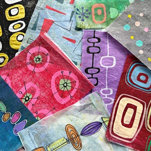 May include: A collection of colorful, patterned paper squares with mid-century modern designs. The patterns include geometric shapes, atomic starbursts, and abstract lines in various colors like red, blue, green, and purple. The papers are layered and overlapping.