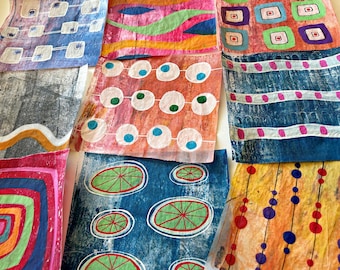 May include: A collection of colorful, patterned fabric squares. Designs include geometric shapes, circles, and organic forms in shades of blue, pink, green, and yellow. The fabric appears to be handmade with a textured, artistic quality.