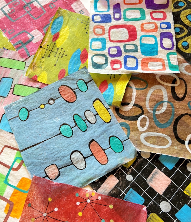 May include: A selection of colourful, patterned paper squares with mid-century modern designs. The squares feature geometric shapes in various colours, including red, blue, yellow, and green. Some have atomic-age inspired designs, while others have abstract patterns.