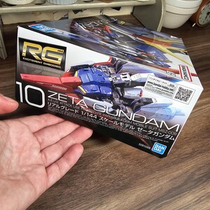 May include: A box for a Zeta Gundam model kit. The box is white with red, blue, and yellow accents. The text "RG" and "10" are prominently displayed. The box also includes Japanese text and the Bandai logo.