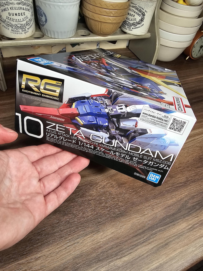 May include: A box for a Zeta Gundam model kit. The box is white with red, blue, and yellow accents. The text "RG" and "10" are prominently displayed. The box also includes Japanese text and the Bandai logo.