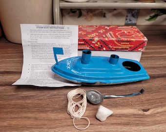 May include: A blue toy steam boat with the word "JACK" printed on the side. The boat has two chimneys and a small flag. The boat is on a wooden surface with a spool of string, a metal lid, and a white rock.