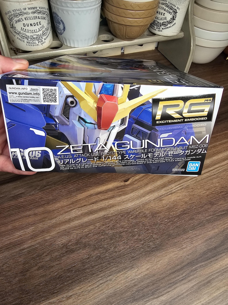 May include: A box for a Zeta Gundam model kit. The box is primarily blue with images of the robot and text in English and Japanese. The box also has the text "RG EXCITEMENT EMBODIED".