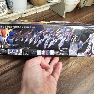 May include: A box for a model kit featuring a detailed illustration of a transforming robot in blue, white, red, and yellow. The box has Japanese text and the words "JAMES KEILLER & SON DUNDEE MARMALADE" on the top left.
