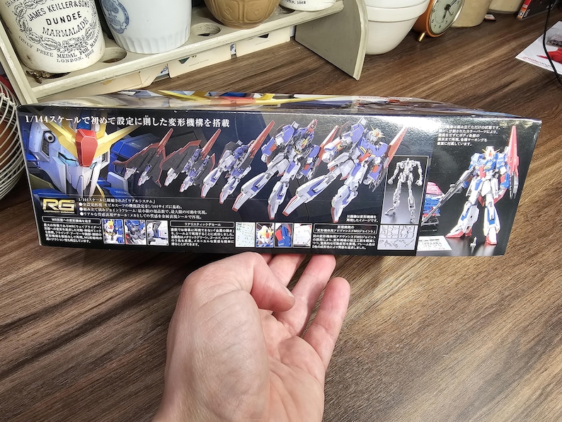 May include: A box for a model kit featuring a detailed illustration of a transforming robot in blue, white, red, and yellow. The box has Japanese text and the words "JAMES KEILLER & SON DUNDEE MARMALADE" on the top left.