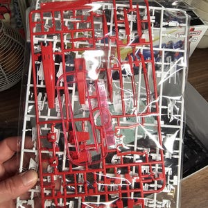 May include: A clear plastic bag containing red and white plastic model kit parts. The parts are attached to a white frame, with various shapes and sizes. The kit appears to be for a robot or vehicle model.