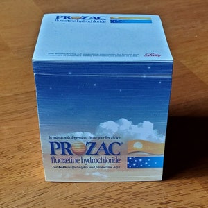 May include: A stack of blue and white notepad paper with the Prozac logo and the text "fluoxetine hydrochloride" and "For both restful nights and productive days".