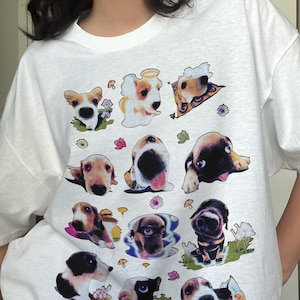 Può includere: Maglietta bianca con una stampa grafica di diversi cani in diverse pose. I cani indossano tutti i colletti e alcuni hanno accessori come cappelli o occhiali da sole.