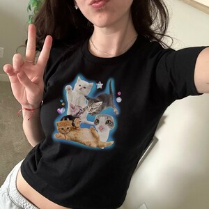 Peut inclure: T-shirt noir &agrave; manches courtes avec un imprim&eacute; de quatre chatons dans une pose ludique. Les chatons sont blancs, gris et orange. L'imprim&eacute; est entour&eacute; de petites &eacute;toiles et de c&oelig;urs.
