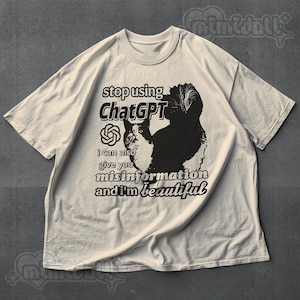 May include: Off-white t-shirt with a black and white cat graphic and text that reads "stop using ChatGPT, I can also give you misinformation and I'm beautiful." The shirt has short sleeves and a crew neck.