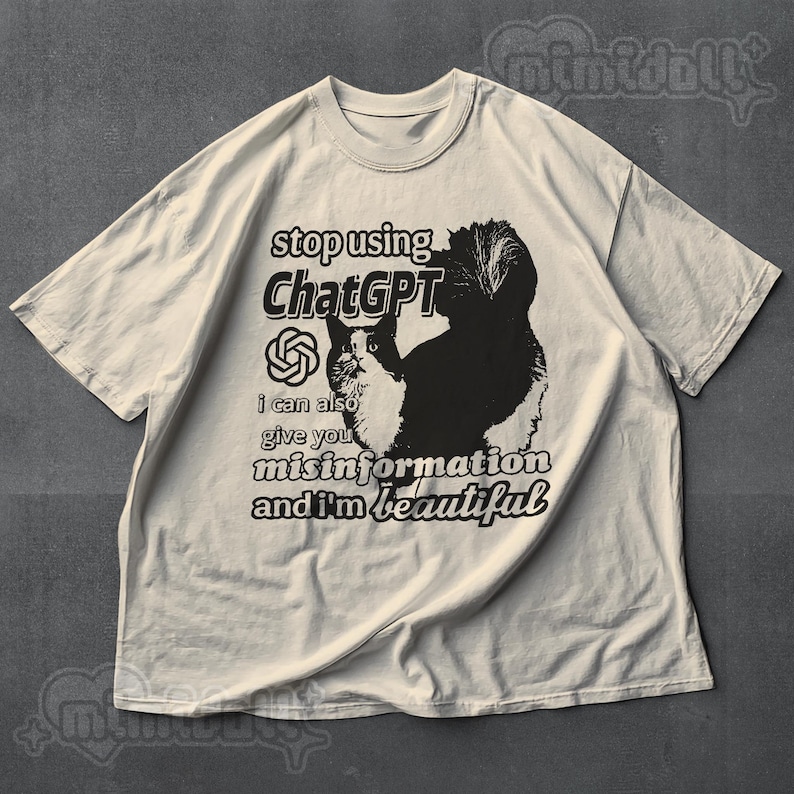 May include: Off-white t-shirt with a black and white cat graphic and text that reads "stop using ChatGPT, I can also give you misinformation and I'm beautiful." The shirt has short sleeves and a crew neck.