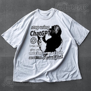 May include: White t-shirt with a black and white cat graphic and the text "stop using ChatGPT, I can also give you misinformation and I'm beautiful." The shirt has a crew neck and short sleeves.