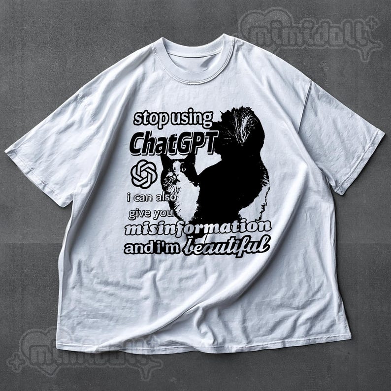 May include: White t-shirt with a black and white cat graphic and the text "stop using ChatGPT, I can also give you misinformation and I'm beautiful." The shirt has a crew neck and short sleeves.