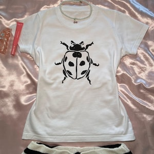 Op de afbeelding: Wit T-shirt met een zwarte lieveheersbeestje print.