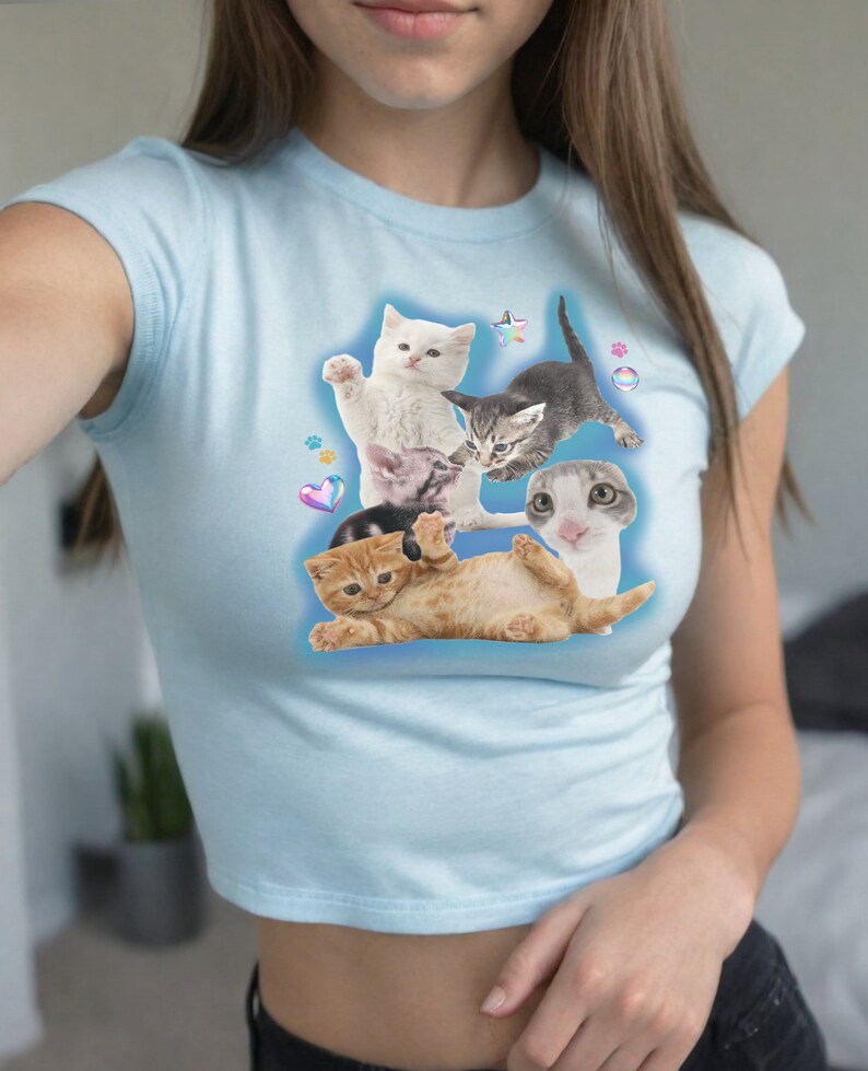 Peut inclure: Un t-shirt court bleu clair avec un imprim&eacute; graphique de plusieurs chatons dans diff&eacute;rentes poses. Les chatons sont blancs, bruns et gris.