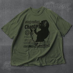 May include: Olive green t-shirt with a black and white cat graphic and text that reads "stop using ChatGPT, I can also give you misinformation and I'm beautiful." The shirt has short sleeves and a crew neck.