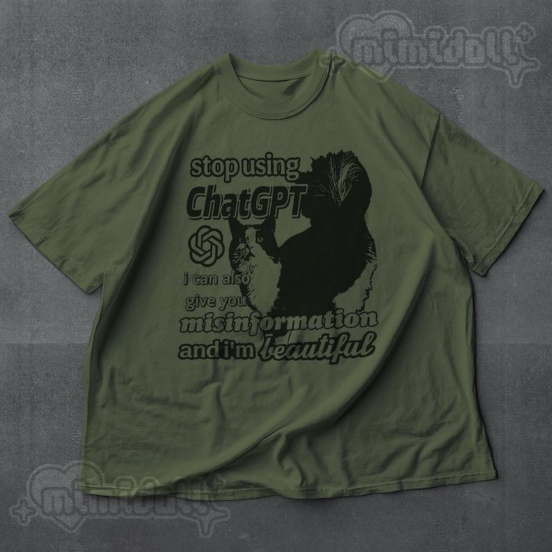 May include: Olive green t-shirt with a black and white cat graphic and text that reads "stop using ChatGPT, I can also give you misinformation and I'm beautiful." The shirt has short sleeves and a crew neck.