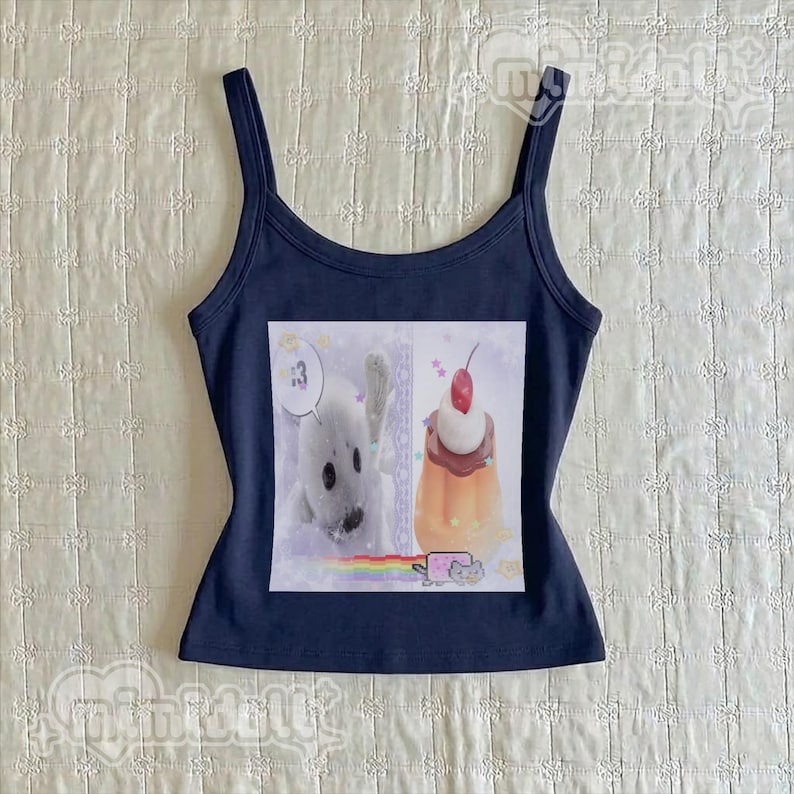 May include: A dark navy blue tank top featuring a square graphic print on the front. The print displays a white seal, a pudding cup topped with a red cherry, a rainbow, and a small cat character. The tank top has a scoop neckline and wide straps.