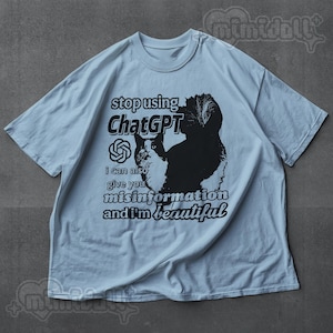 May include: Light blue t-shirt with a graphic of a cat and the text "stop using ChatGPT, I can also give you misinformation and I'm beautiful." The cat is black and white.