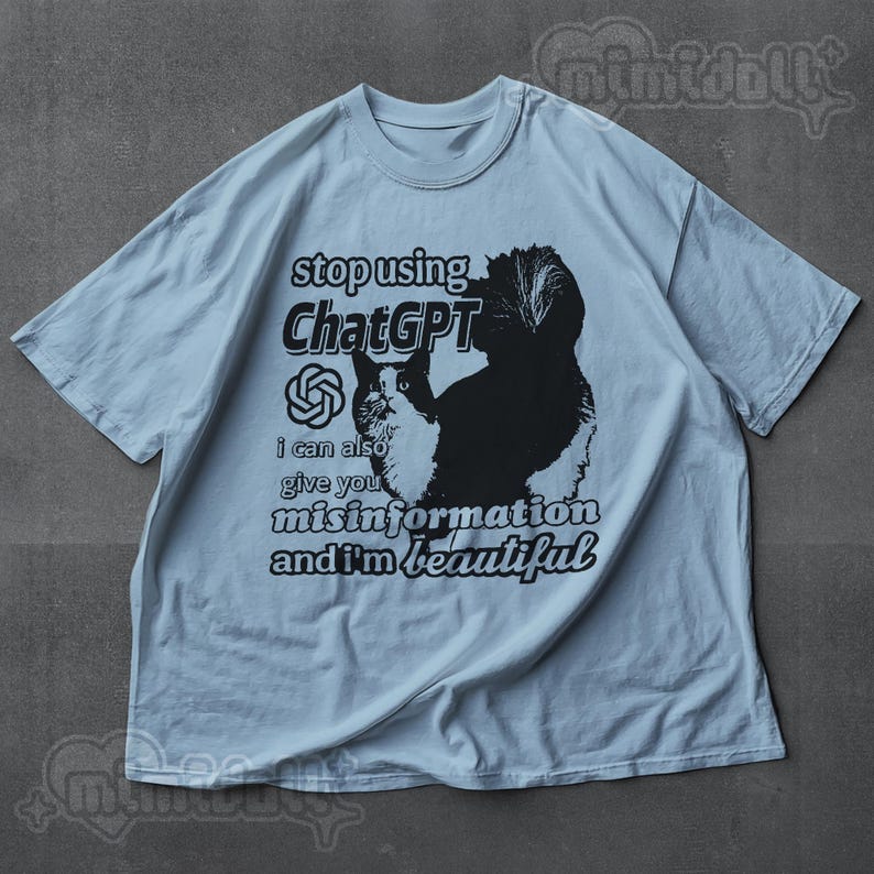 May include: Light blue t-shirt with a graphic of a cat and the text "stop using ChatGPT, I can also give you misinformation and I'm beautiful." The cat is black and white.
