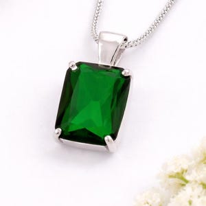 May include: A silver-toned necklace featuring a rectangular, emerald-green gemstone pendant. The pendant is held by a simple metal bail and hangs from a delicate silver-toned chain. The design is clean, focusing on the vibrant green stone.