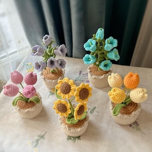 Peut inclure: Plusieurs arrangements floraux crochetés à la main. Les compositions comprennent des tulipes, des tournesols et des fleurs en forme de cloche dans diverses couleurs, comme le rose, le jaune et le bleu. Chaque fleur est dans un petit panier tissé.