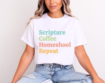 May include: White t-shirt featuring the text "Scripture Coffee Homeschool Repeat" in teal, green, coral, and yellow. The shirt is a casual, short-sleeved style.