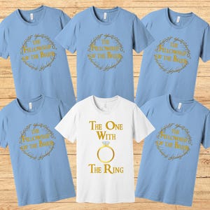 May include: Set of six light blue t-shirts with gold text and graphics. The shirts feature the text "The Fellowship of the Bride" and "The One with the Ring".