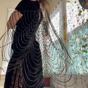 Può includere: Un abito in velluto nero con un design a ragnatela di perline. L'abito ha uno spacco laterale ed è abbinato a collant a rete neri.
