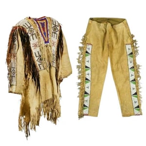 Puede incluir: Un atuendo de ante de color beige, que incluye un poncho con flecos y pantalones. El poncho presenta intrincados abalorios en blanco, azul, rojo y marrón. Los pantalones tienen detalles laterales con cuentas y flecos.