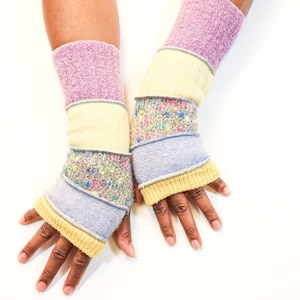 May include: A pair of colorful fingerless gloves. The gloves are made of various knit fabrics in shades of lavender, yellow, blue, and floral patterns. The gloves are designed to cover the wrist and part of the hand, leaving the fingers exposed.