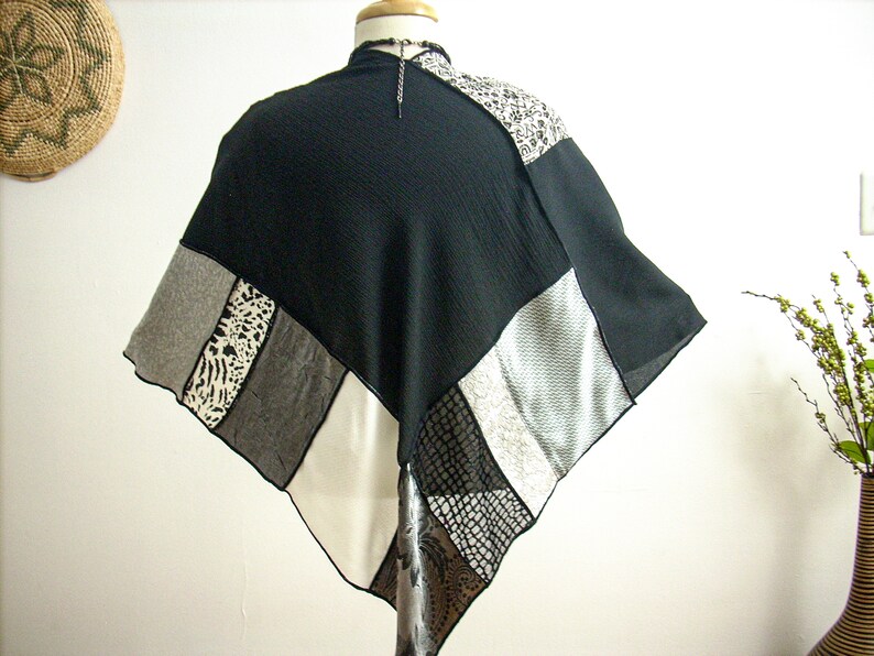 K&ouml;nnte beinhalten: Ein schwarzer, wei&szlig;er und grauer Patchwork-Poncho mit geometrischem Muster. Der Poncho besteht aus verschiedenen Stoffen, darunter ein durchsichtiger Stoff, ein Strickstoff und ein gewebter Stoff.