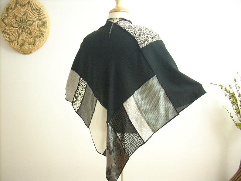 K&ouml;nnte beinhalten: Ein schwarz-wei&szlig;es Patchwork-Poncho mit geometrischem Muster. Das Poncho besteht aus verschiedenen Stoffen, darunter durchsichtige und strukturierte Materialien.