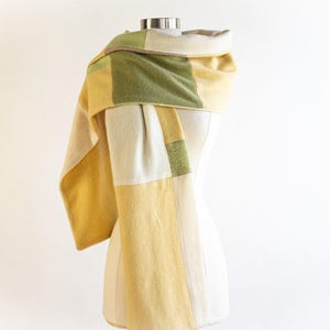 May include: A yellow, green, and white patterned scarf made of soft fabric. The scarf is draped around a mannequin's neck.